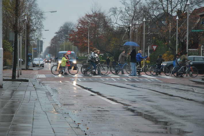 Overstekende kinderen fietsers en iemand die het verkeer tegenhoud in de regen